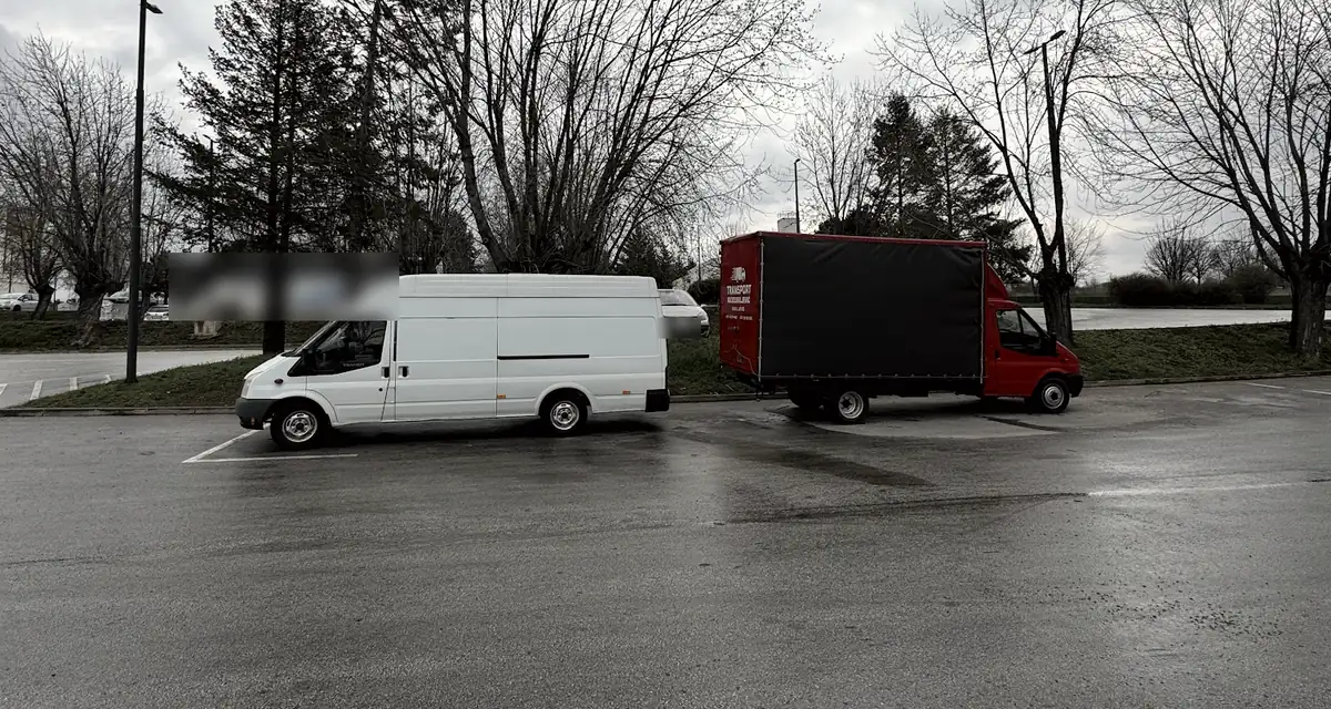 Beli kombi i crveni kamion na mokrom parkingu